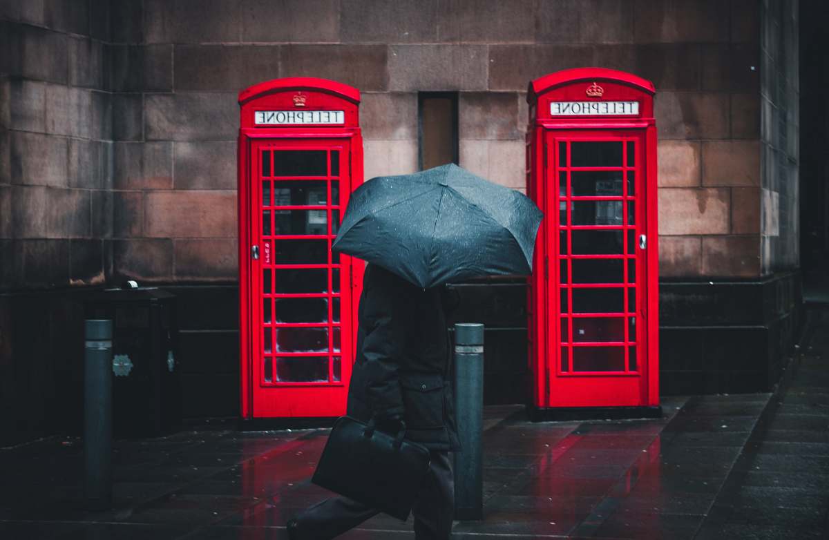 umbrella person under umbrella walking beside telephone booths manchester